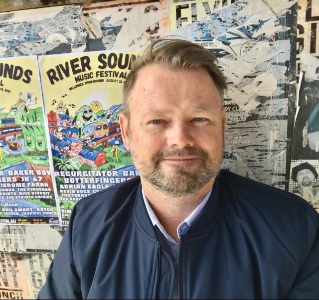 Festival Director_Ben Lewis Ben Lewis in front of River Sounds poster