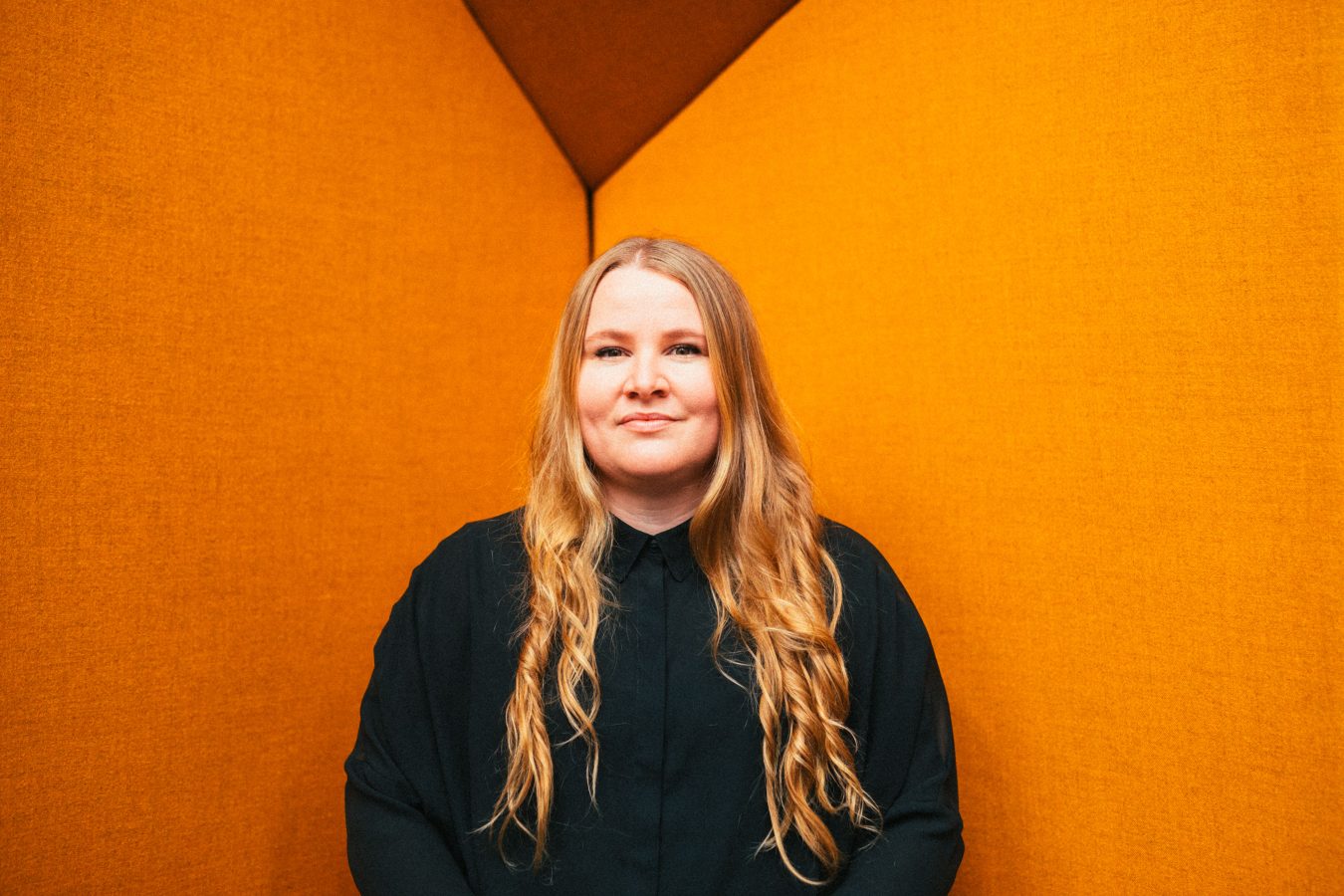 Emily Collins of Music NSW is looking straight at the camera. She is standing against an orange wall.